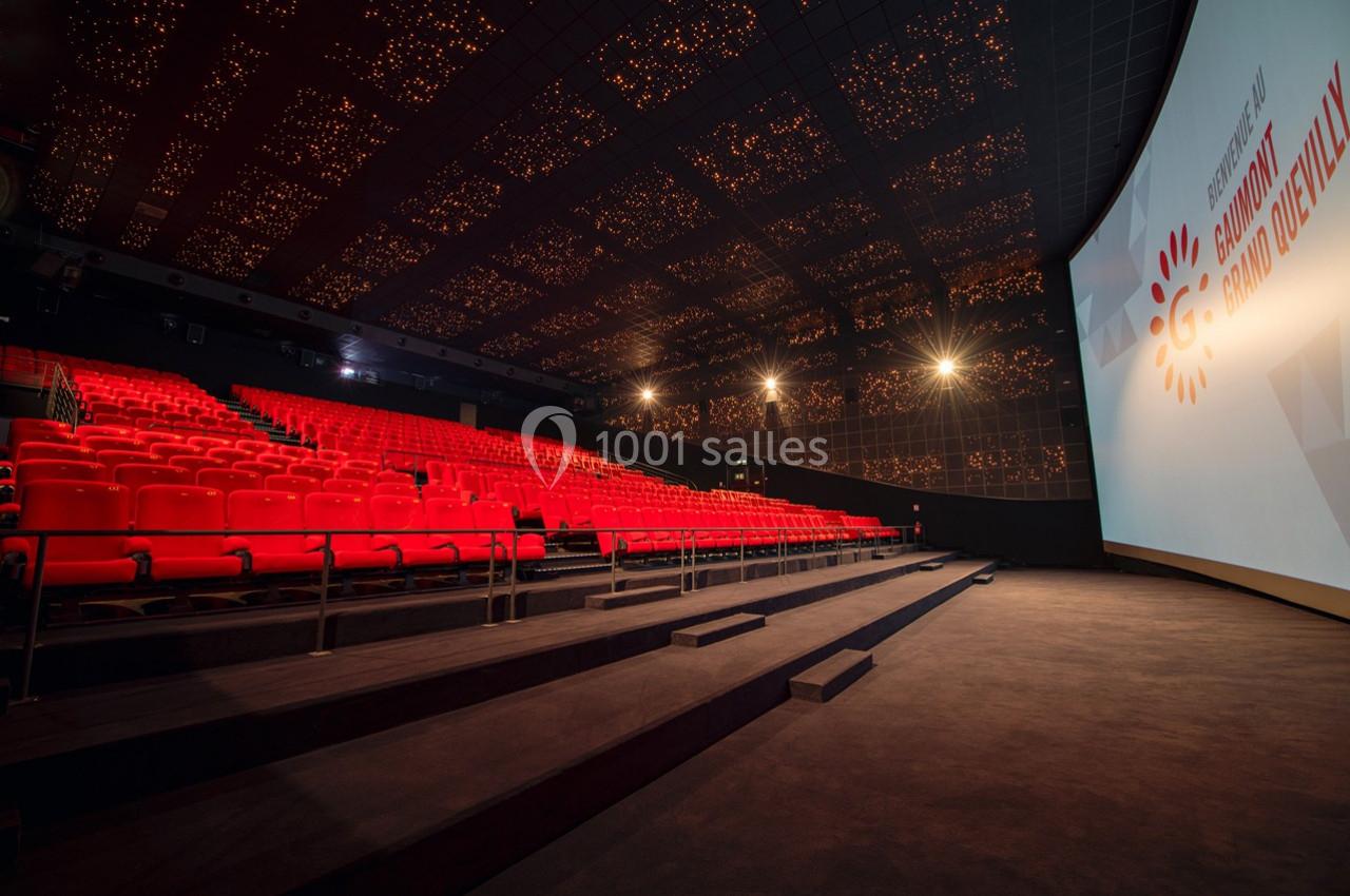 Salle de cinéma vide avec fauteuils rouges, grand écran allumé et plafond illuminé par des motifs lumineux.