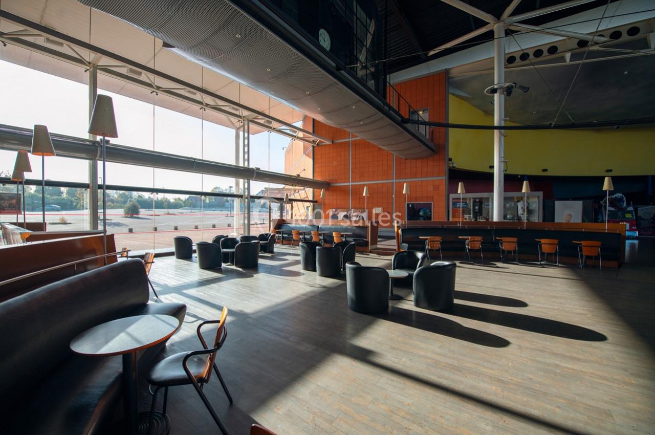 Espace intérieur lumineux avec tables, chaises et grandes baies vitrées donnant sur l'extérieur.