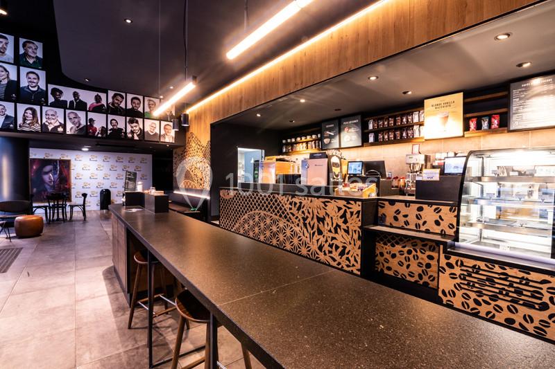 Intérieur d'un café moderne avec comptoir en bois décoré, vitrines réfrigérées et portraits accrochés au mur.