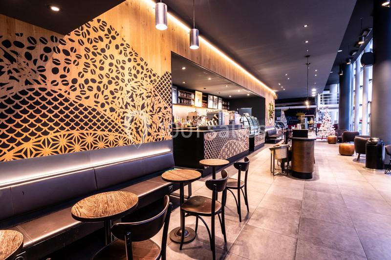 Intérieur d'un café moderne avec des tables en bois, un comptoir décoré et un éclairage chaleureux.