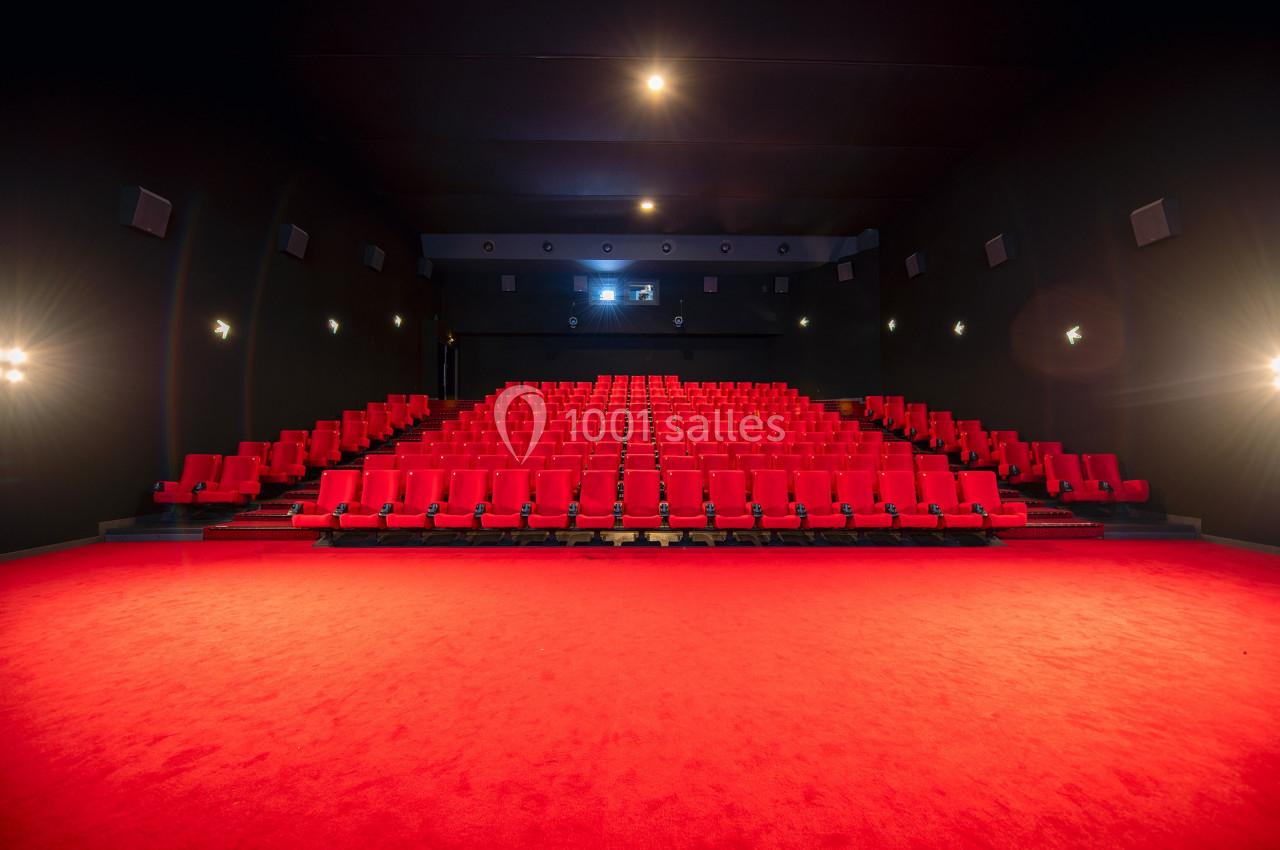 Salle de cinéma vide avec rangées de sièges rouges et éclairage tamisé.