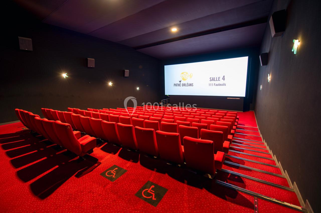 Salle de cinéma vide avec rangées de sièges rouges, écran allumé et espaces réservés aux personnes à mobilité réduite au…