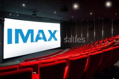 Façade d'un cinéma IMAX moderne avec parking vide au premier plan et ciel nuageux en arrière-plan.