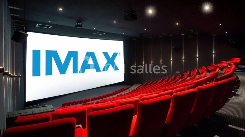 Salle de cinéma IMAX avec écran géant, rangées de sièges rouges et éclairage tamisé.