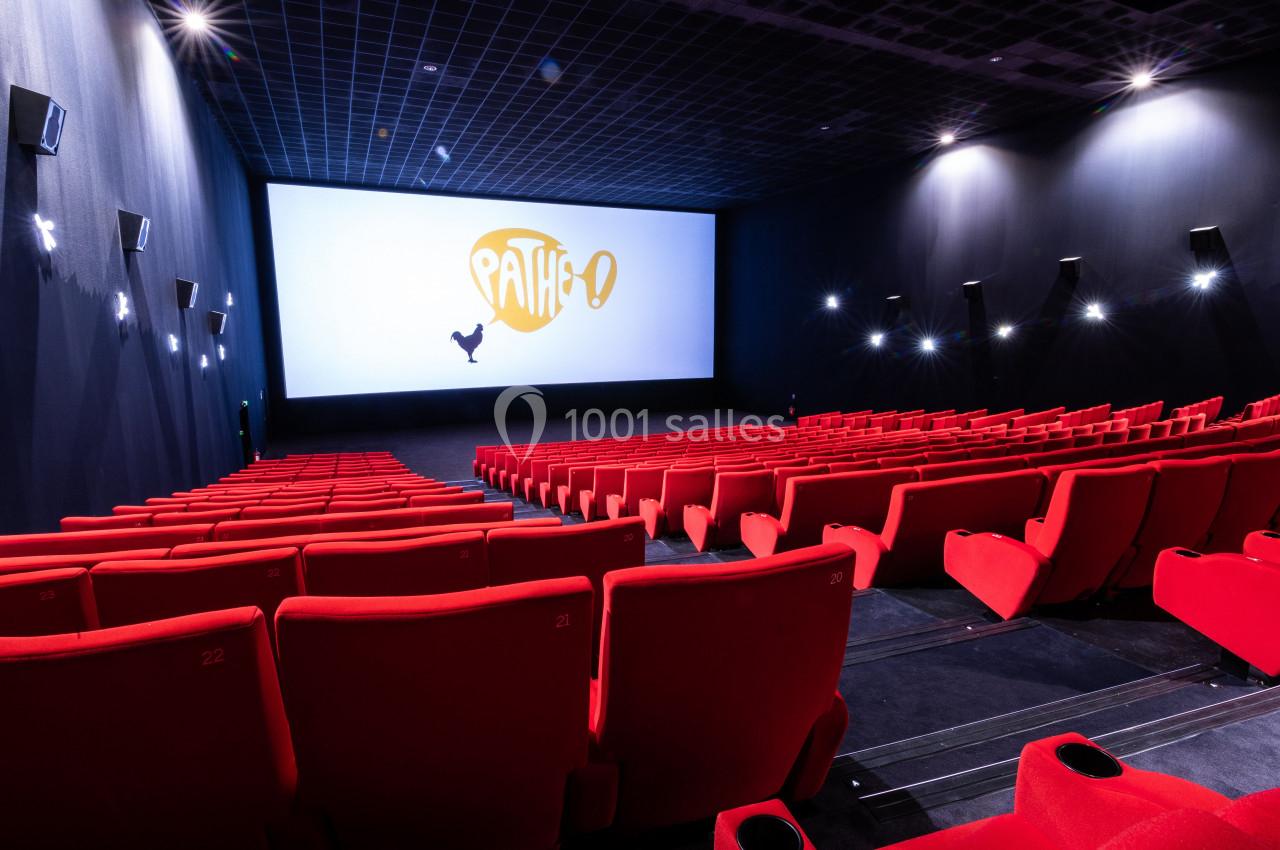 Salle de cinéma vide avec des sièges rouges, un grand écran allumé affichant le logo Pathé.