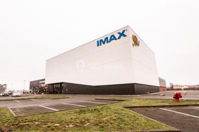 Façade d'un cinéma IMAX moderne avec parking vide au premier plan et ciel nuageux en arrière-plan.