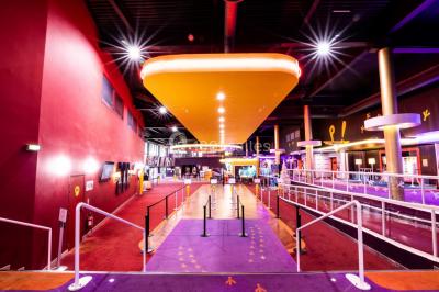 Façade d'un cinéma IMAX moderne avec parking vide au premier plan et ciel nuageux en arrière-plan.