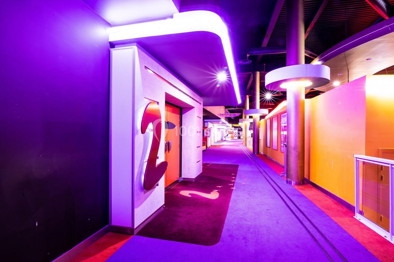 Couloir intérieur coloré avec éclairage néon violet, moquette rouge et violet, et signalisation murale indiquant ’2’.