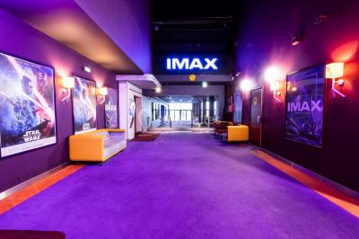 Façade d'un cinéma IMAX moderne avec parking vide au premier plan et ciel nuageux en arrière-plan.