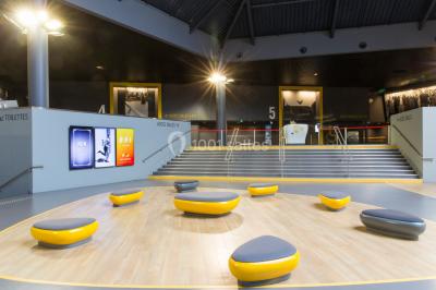 Salle de cinéma vide avec des rangées de sièges rouges et un grand écran blanc allumé.