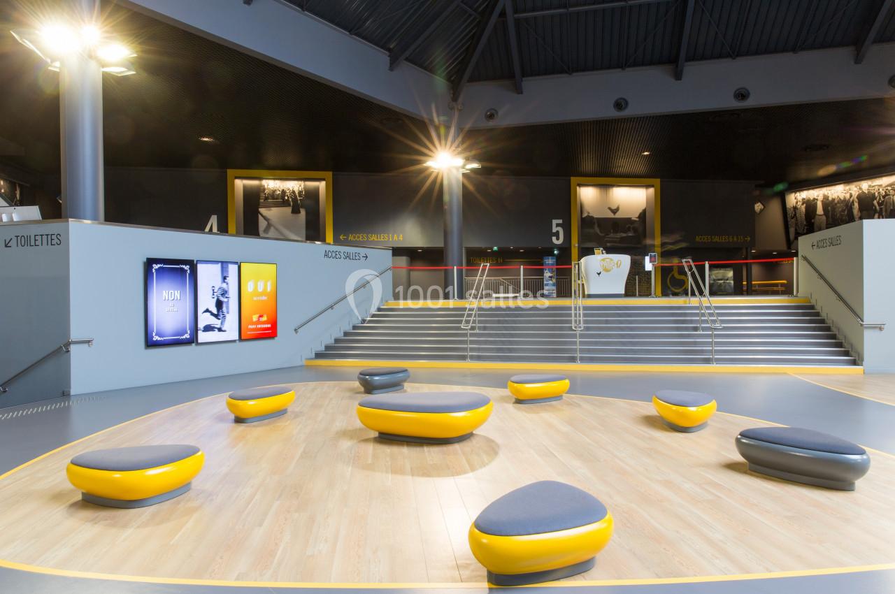 Espace intérieur moderne avec sièges arrondis jaunes et gris, escalier en arrière-plan et panneaux lumineux.