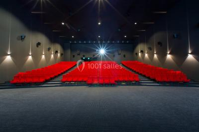 Salle de cinéma vide avec des rangées de sièges rouges et un grand écran blanc allumé.