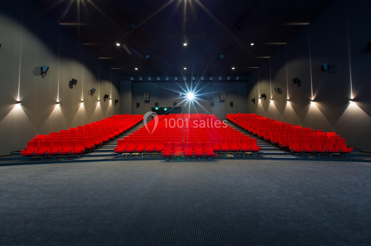 Salle de cinéma vide avec des rangées de sièges rouges et un projecteur allumé au fond.