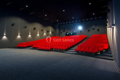 Salle de cinéma vide avec des rangées de sièges rouges et un grand écran blanc allumé.