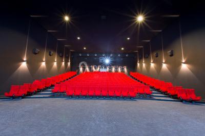 Salle de cinéma vide avec des rangées de sièges rouges et un grand écran blanc allumé.