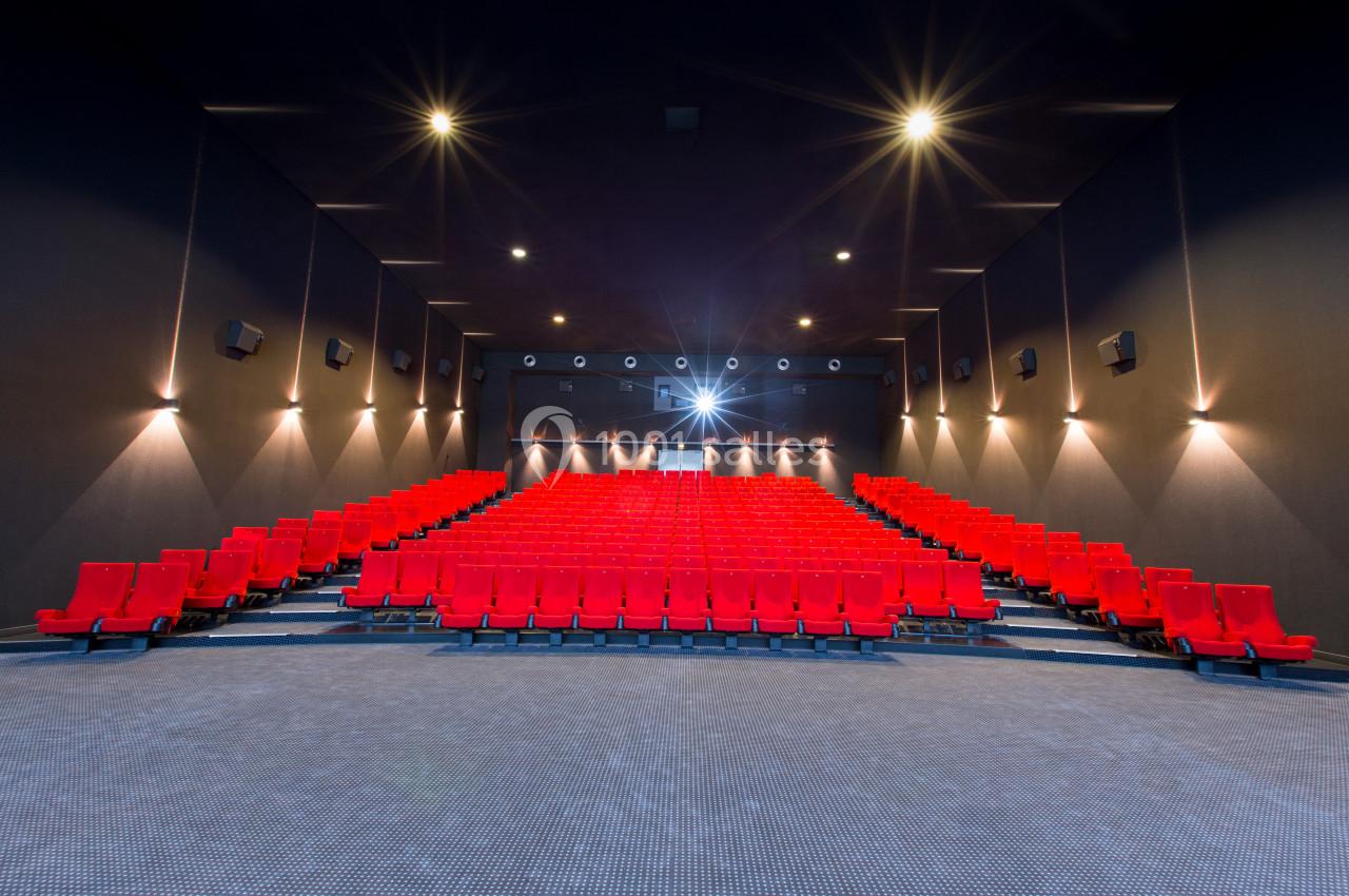 Salle de cinéma vide avec des rangées de sièges rouges et un écran blanc éclairé au fond.