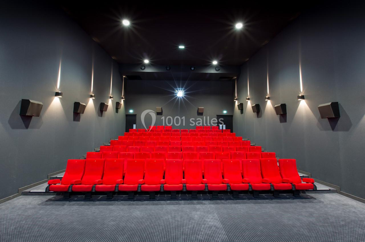 Salle de cinéma vide avec rangées de sièges rouges alignés et éclairage tamisé sur les murs gris.