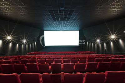 Salle de cinéma avec sièges rouges et grand écran affichant le logo IMAX, éclairage tamisé.