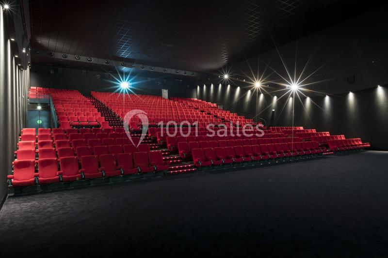 Salle de cinéma vide avec des rangées de sièges rouges et un éclairage tamisé.
