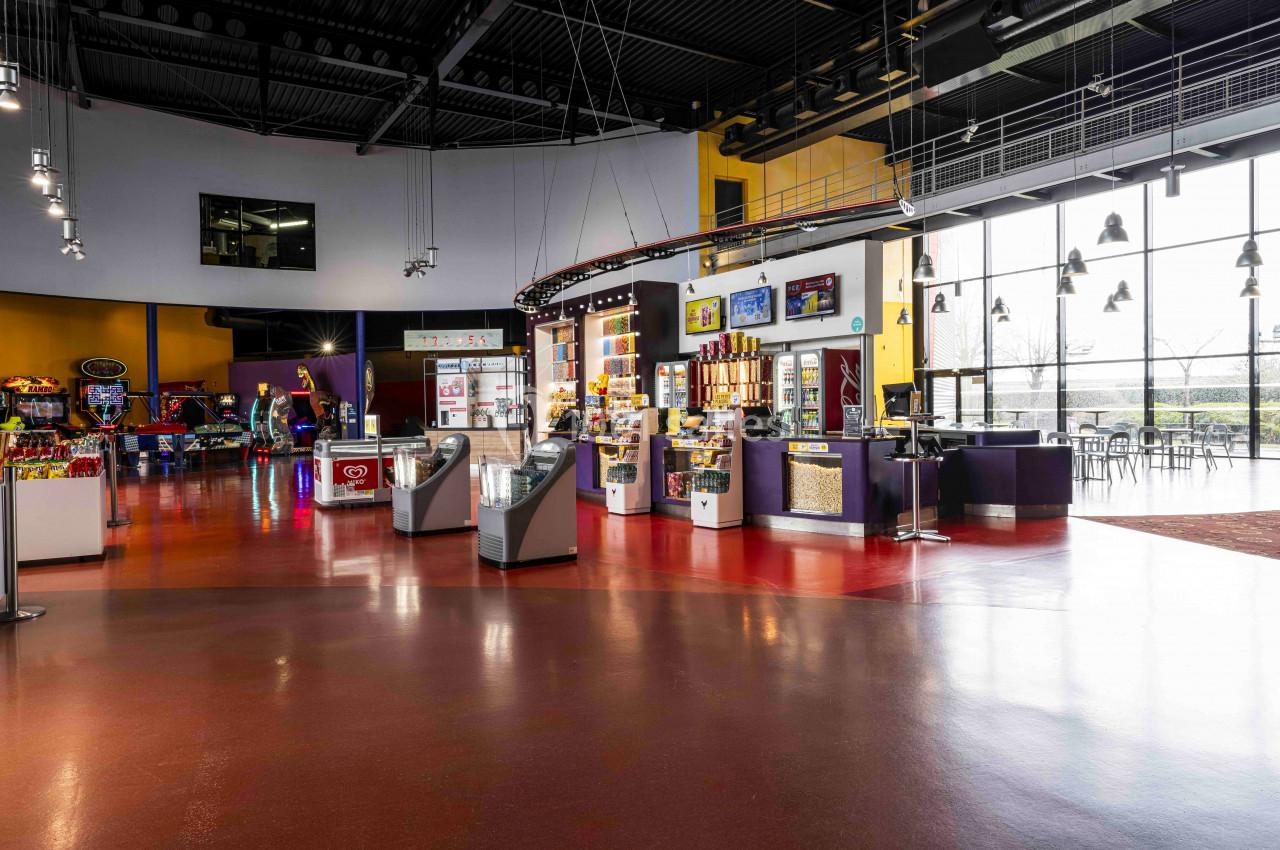Espace intérieur lumineux avec sol rouge, stands de confiserie, jeux d'arcade et grandes baies vitrées donnant sur l…