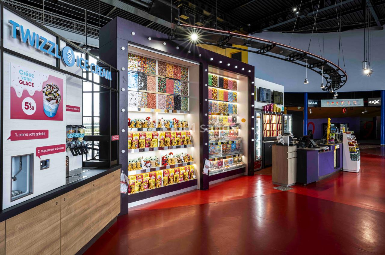 Mur coloré de bonbons en libre-service avec distributeurs, présentoirs lumineux et comptoir de caisse dans un espace…