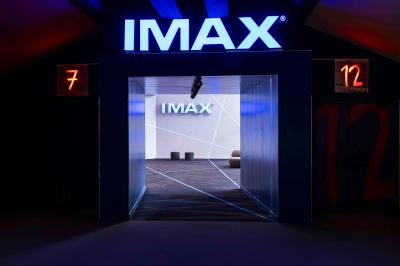 Salle de cinéma avec sièges rouges et grand écran affichant le logo IMAX, éclairage tamisé.