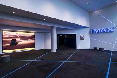 Salle de cinéma avec sièges rouges et grand écran affichant le logo IMAX, éclairage tamisé.