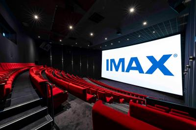 Salle de cinéma avec sièges rouges et grand écran affichant le logo IMAX, éclairage tamisé.