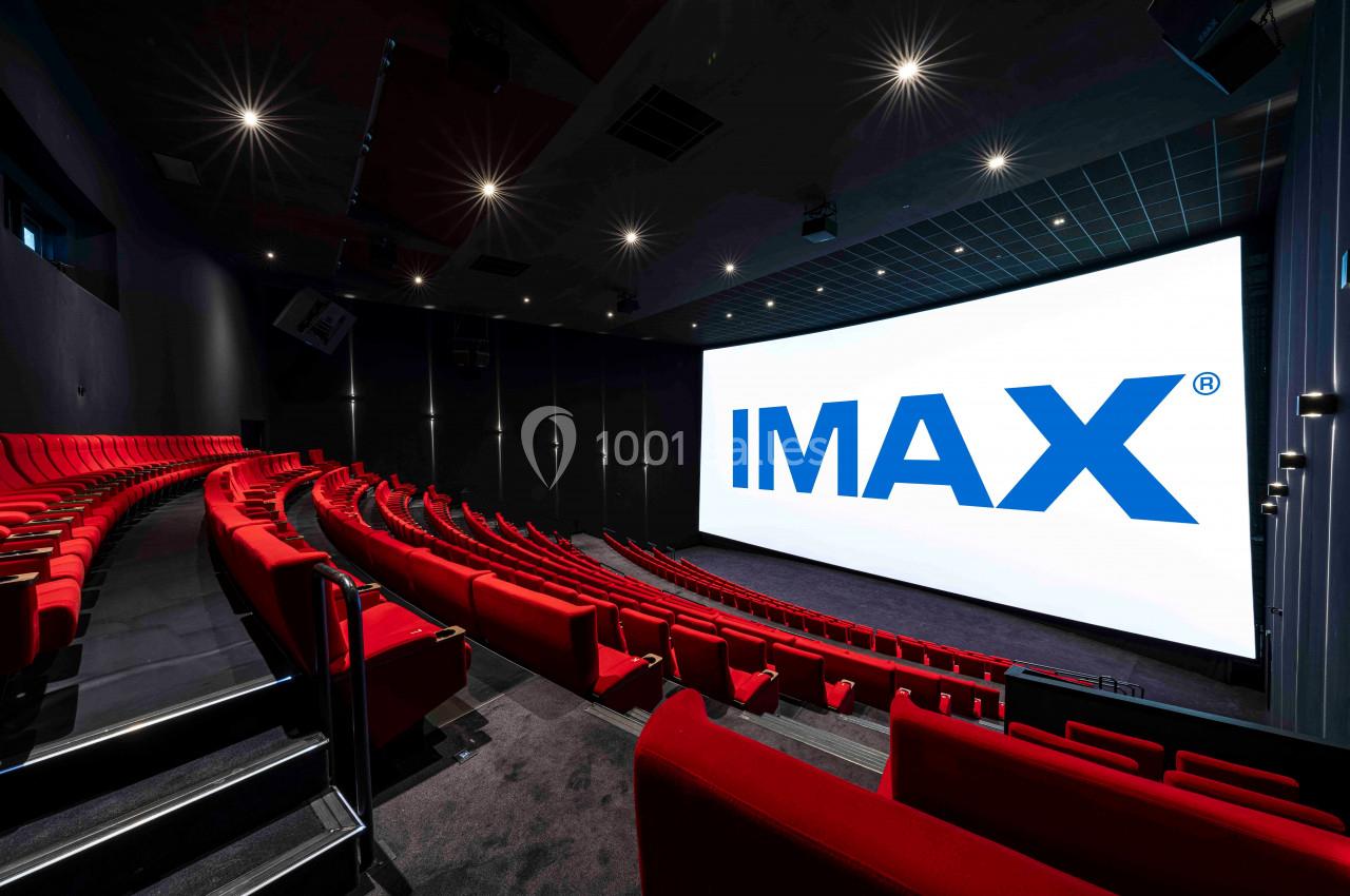 Salle de cinéma avec sièges rouges et grand écran affichant le logo IMAX, éclairage tamisé.