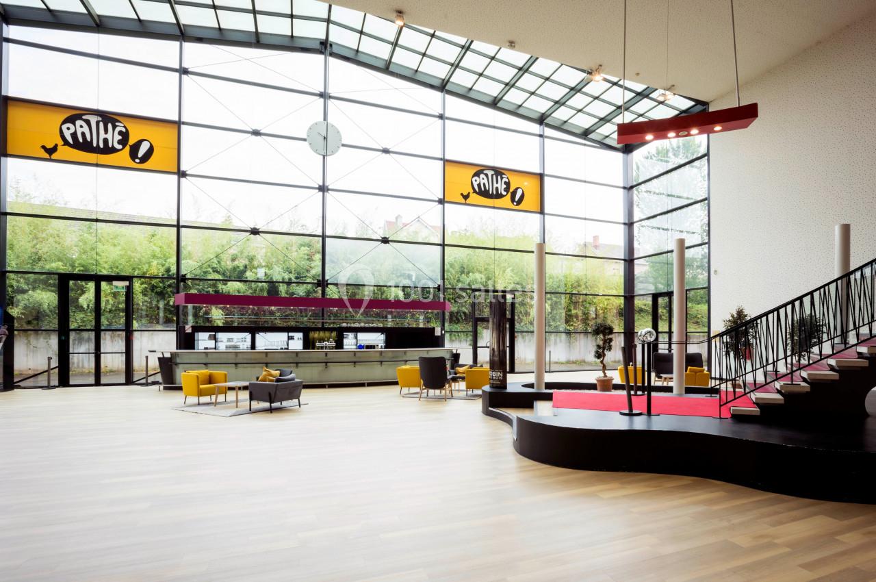 Hall spacieux avec grandes baies vitrées, escalier moderne, mobilier jaune et comptoir d'accueil sous enseignes Pathé.