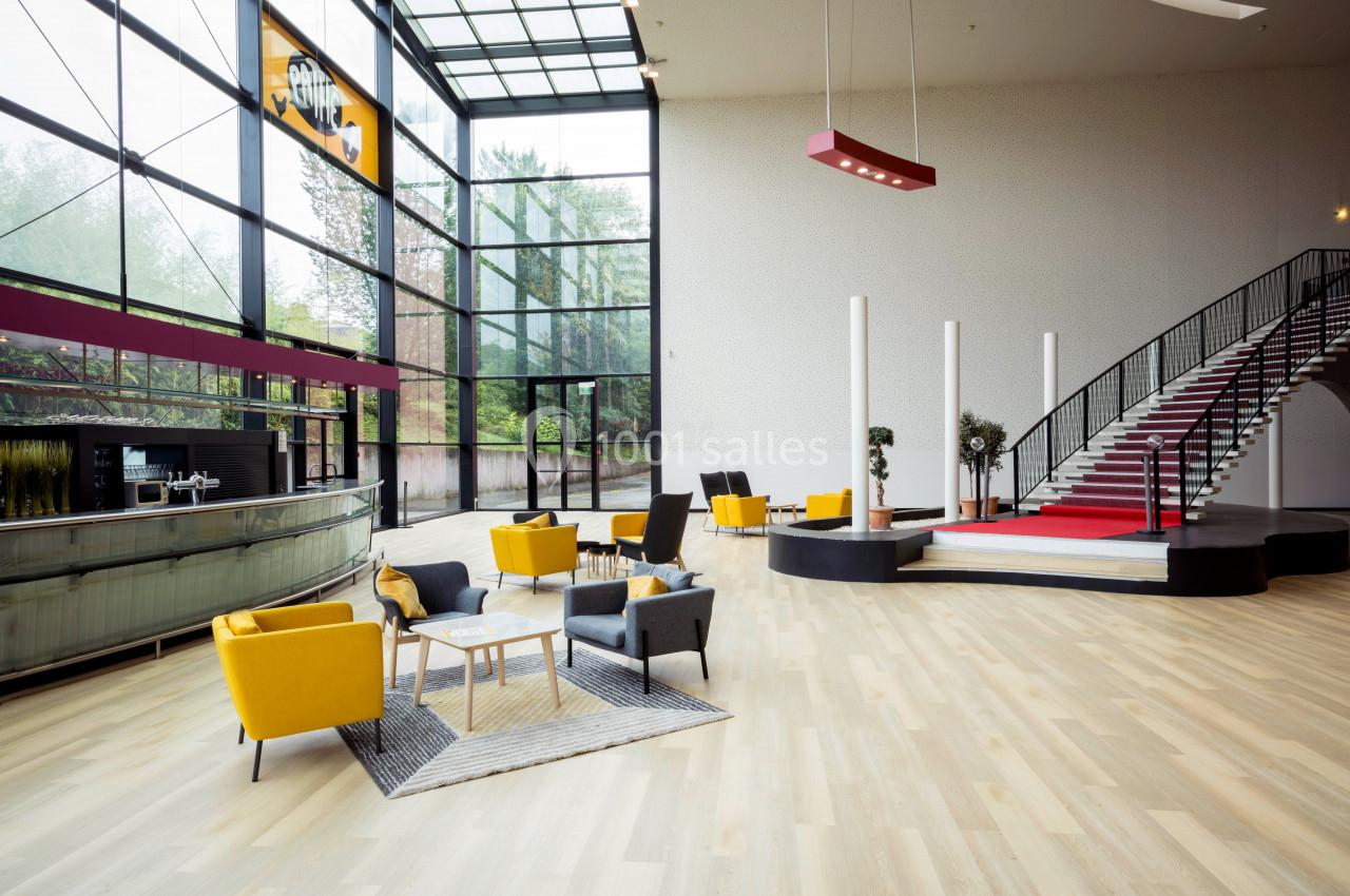 Intérieur lumineux avec escalier, mobilier moderne coloré et grandes baies vitrées donnant sur un espace arboré.