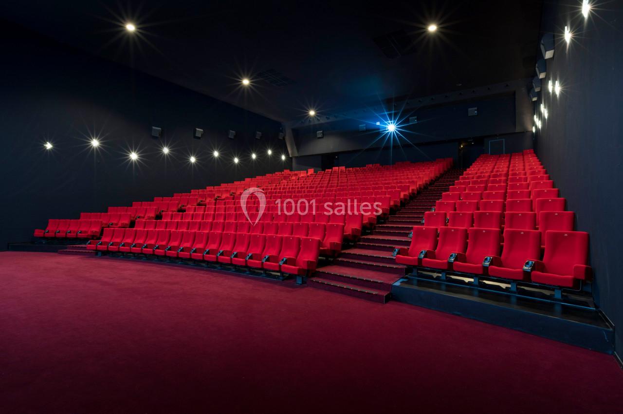 Salle de cinéma vide avec rangées de fauteuils rouges, éclairage tamisé et écran hors champ.