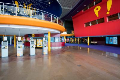 Escalier mécanique dans un espace intérieur moderne avec moquette violette, plafonds hauts et enseignes lumineuses.