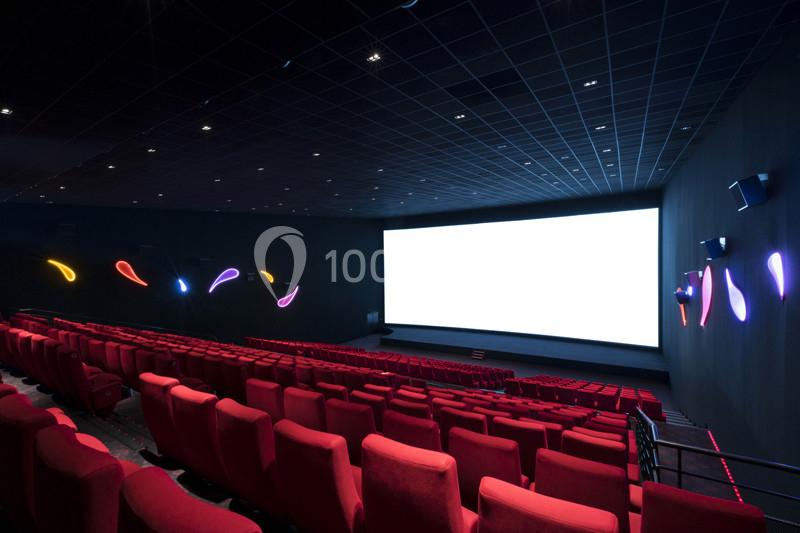 Salle de cinéma vide avec des rangées de sièges rouges, un grand écran blanc et des lumières colorées sur les murs.