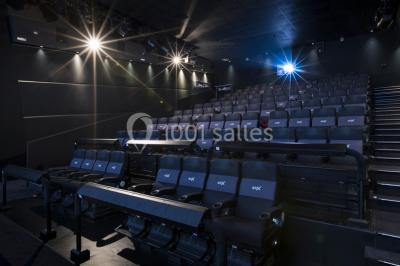 Salle de cinéma moderne avec sièges inclinables, éclairage tamisé et projecteur allumé.