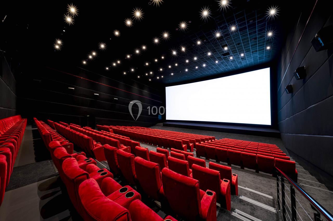 Salle de cinéma vide avec des rangées de fauteuils rouges et un grand écran blanc allumé.