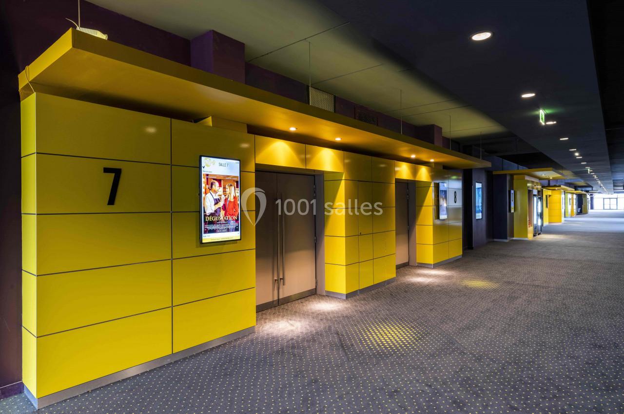 Couloir de cinéma avec des portes numérotées et des affiches de films sur des murs jaunes.