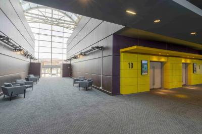 Couloir lumineux avec moquette grise, fauteuils, murs sombres, panneaux jaunes et ascenseurs numérotés 10.