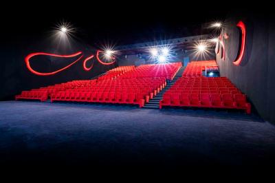 Façade d'un cinéma Pathé illuminée au crépuscule, avec des bâtiments en arrière-plan et des traînées lumineuses de voitures.