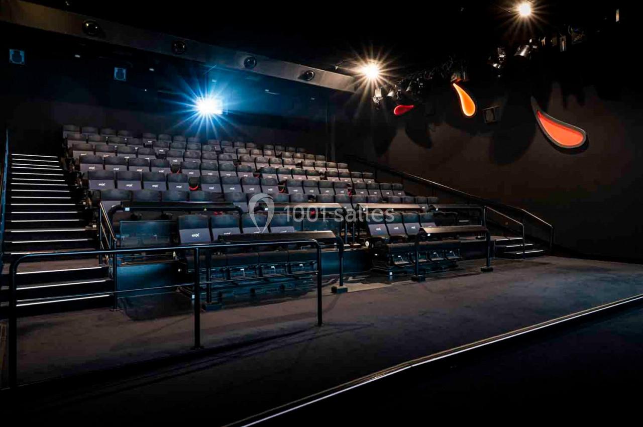 Salle de cinéma vide avec rangées de sièges, éclairage tamisé et projecteur allumé.