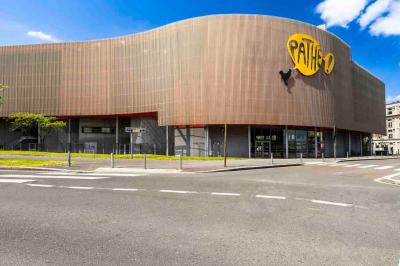 Façade d'un cinéma Pathé illuminée au crépuscule, avec des bâtiments en arrière-plan et des traînées lumineuses de voitures.