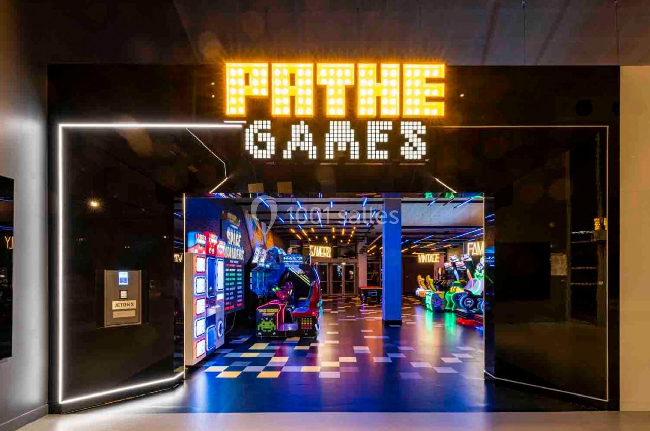Entrée d'une salle d'arcade moderne avec enseigne lumineuse ’Pathé Games’ et jeux colorés à l'intérieur.