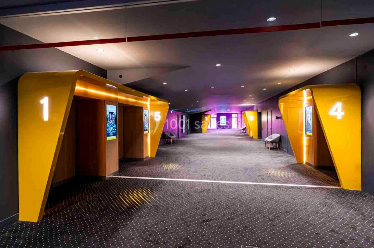 Couloir d'un cinéma avec des entrées de salles numérotées en jaune et éclairage tamisé.