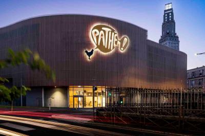 Façade d'un cinéma Pathé illuminée au crépuscule, avec des bâtiments en arrière-plan et des traînées lumineuses de voitures.