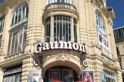 Façade d'un cinéma Gaumont avec des affiches de films et des parasols rouges devant l'entrée.