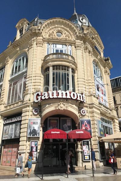Façade d'un cinéma Gaumont avec des affiches de films et des parasols rouges devant l'entrée.