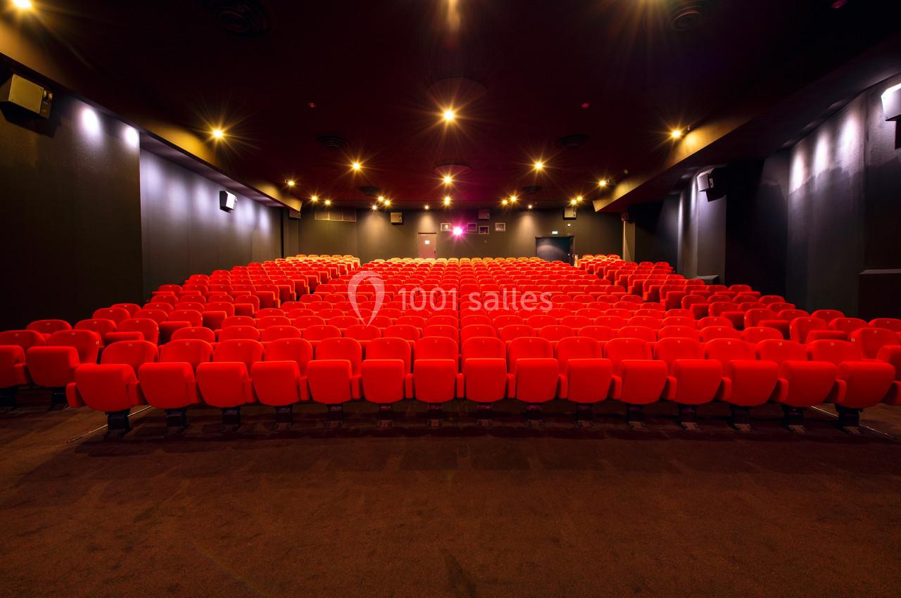 Salle de cinéma vide avec des rangées de fauteuils rouges alignés et un éclairage tamisé.