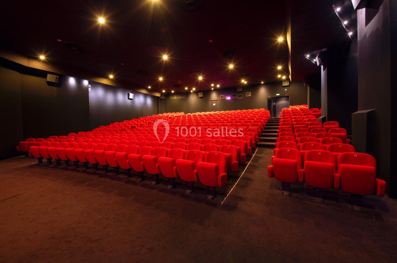 Salle de cinéma vide avec des rangées de sièges rouges et un éclairage tamisé.