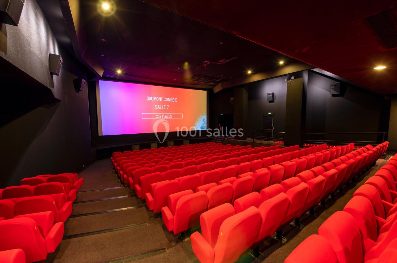 Salle de cinéma vide avec des rangées de sièges rouges et un écran affichant ’Gaumont Comédie Salle 7’.