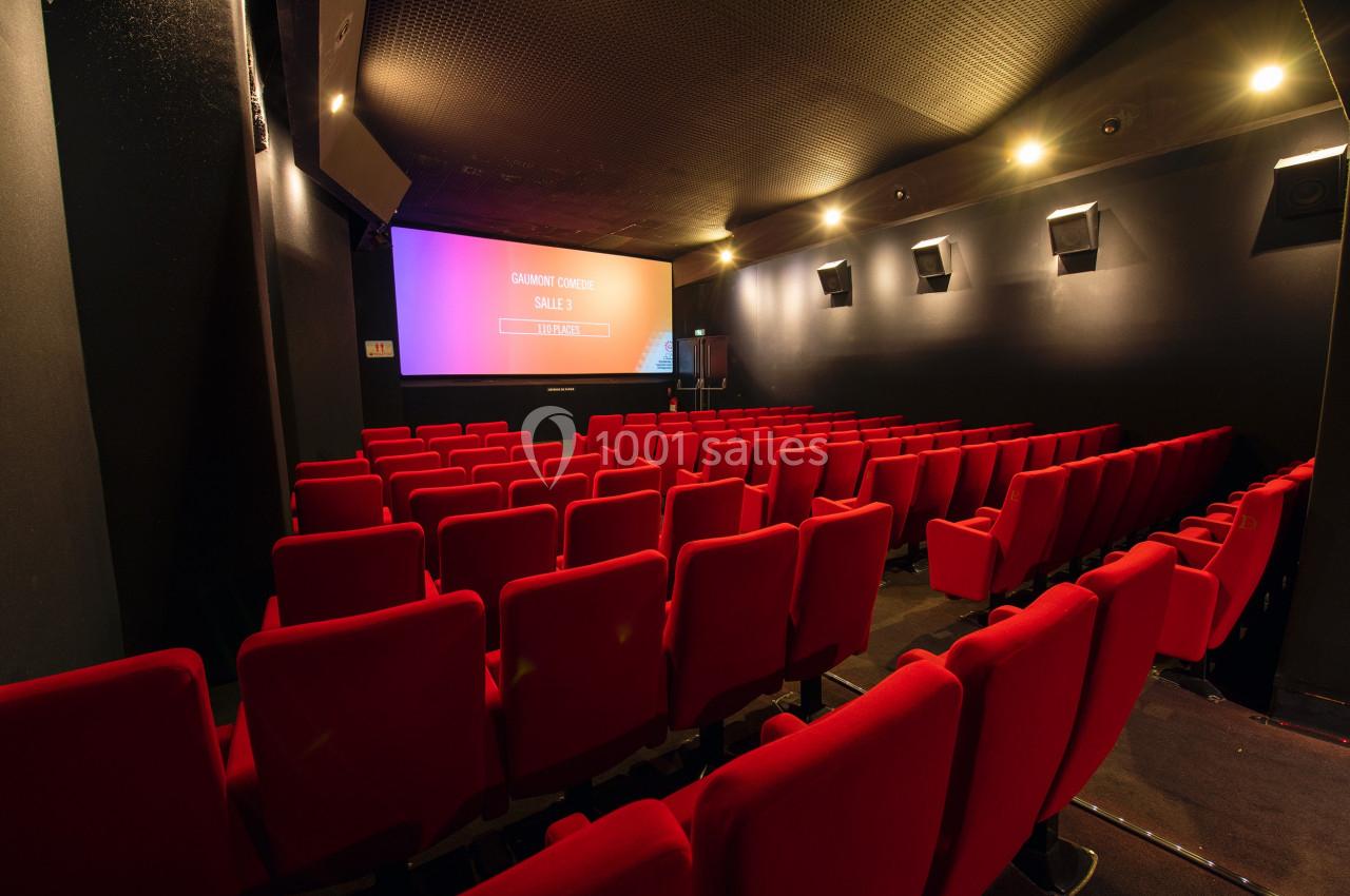 Salle de cinéma vide avec rangées de sièges rouges et écran allumé affichant des informations.